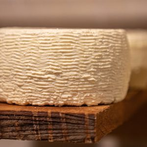 Detailed close-up of a textured cheese wheel maturing on a wooden shelf, highlighting its artisanal nature.